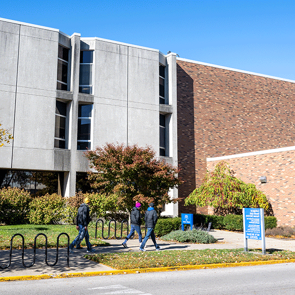 Three students walk past the front of the ISU Health Center building on a summer day.